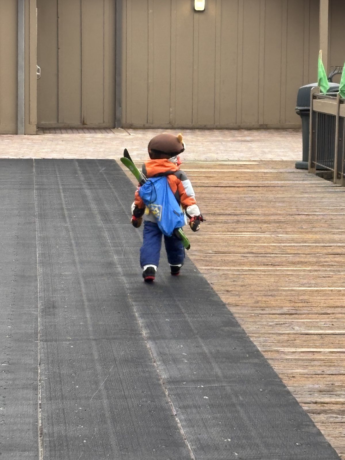 A young Ski Club student walking toward the lodge, skis over one shoulder and a gear bag on their back.