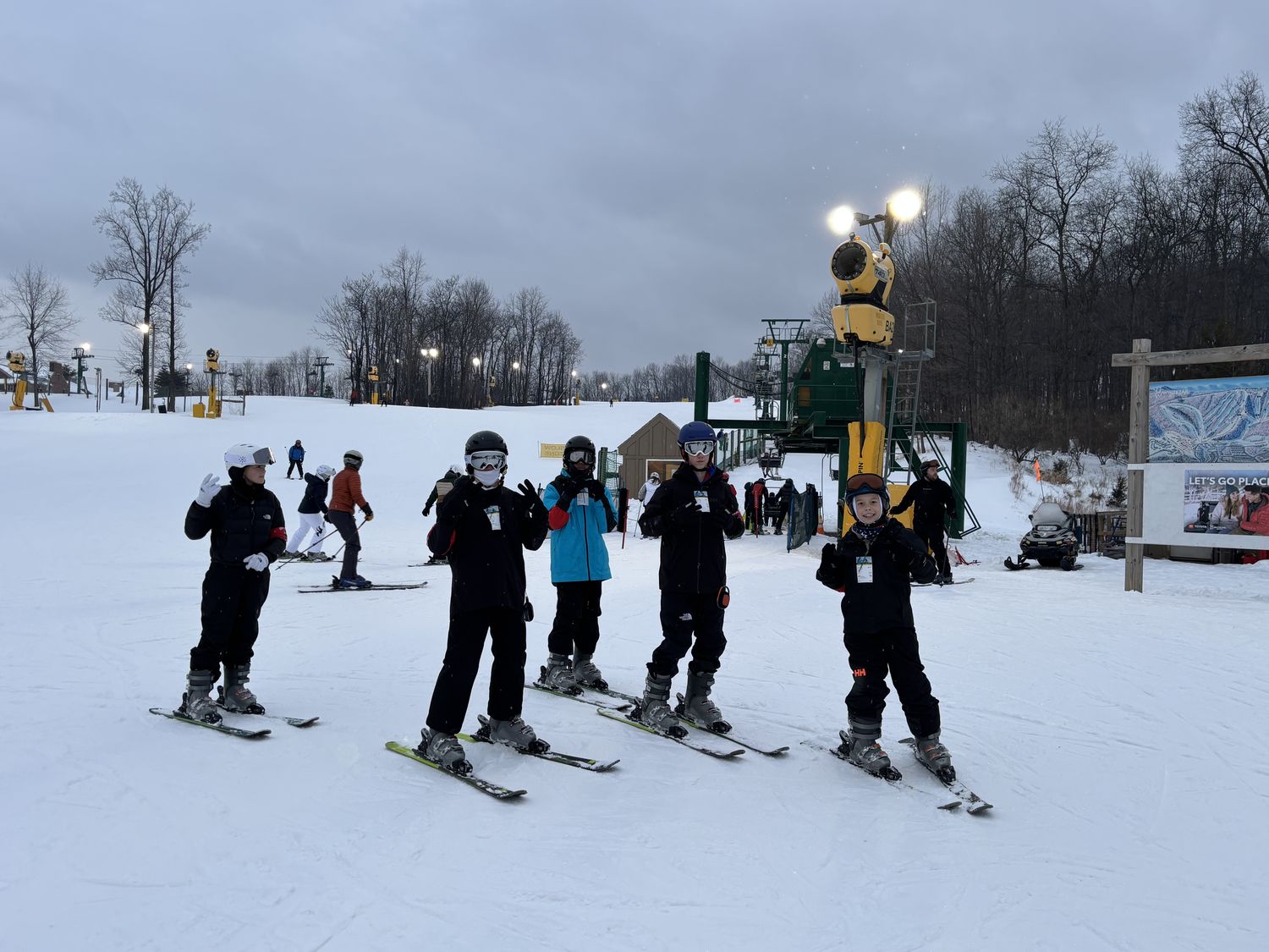 Five Ski Club students in helmets and goggles gathered on their skis at the base of the lift.