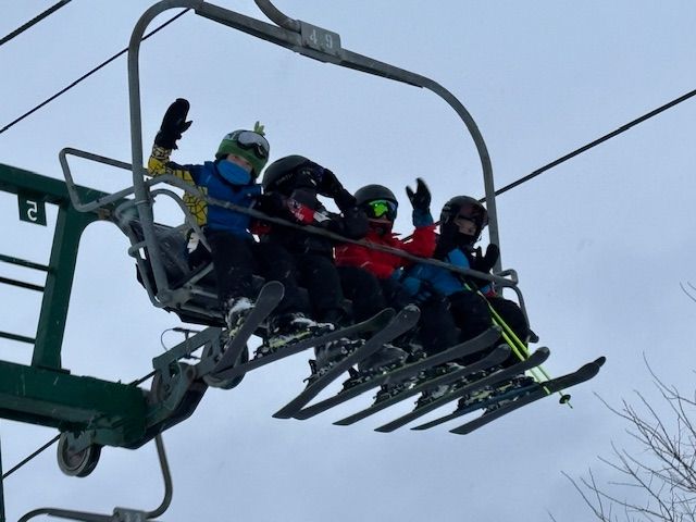 Four students waving from a chairlift high above the slope.